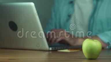 年轻人用笔记本电脑打字。 绿苹果在桌子上。